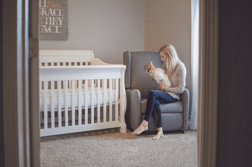 Picture shot through doorway of woman holding baby in arms while sitting in nursery.